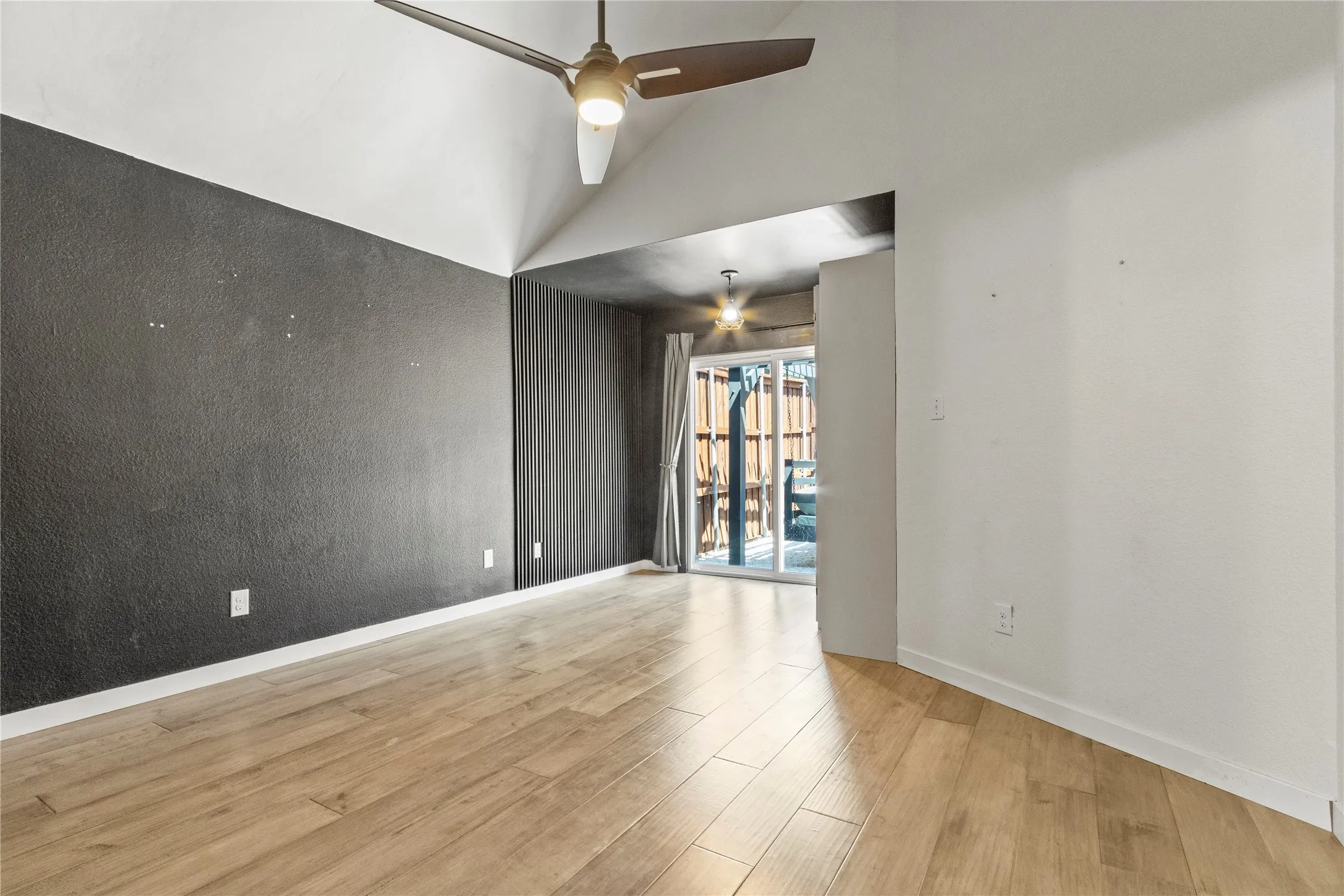 Vaulted ceiling with a ceiling fan, wood-finish flooring, and sliding glass doors