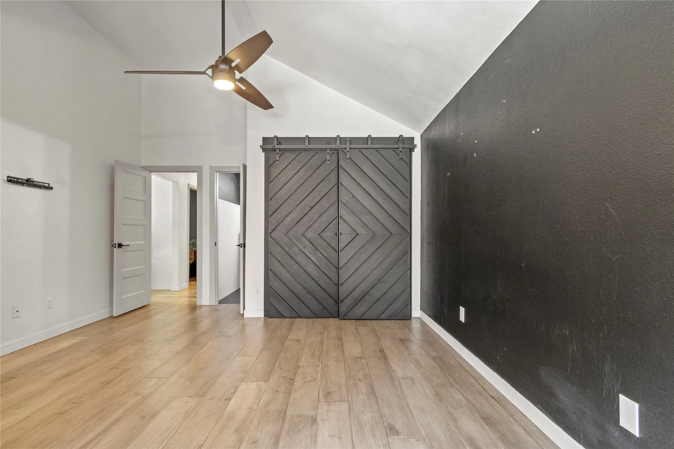 Vaulted ceiling with a contemporary ceiling fan, wood-finish flooring, and a textured accent wall