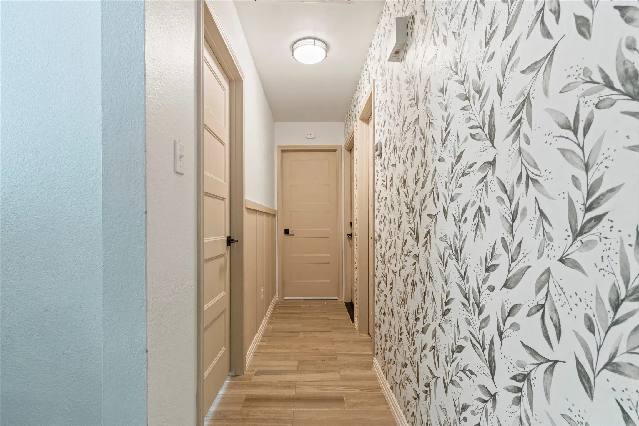 Hallway featuring wood-finish flooring, two-panel doors, decorative wallpaper, and wainscoting