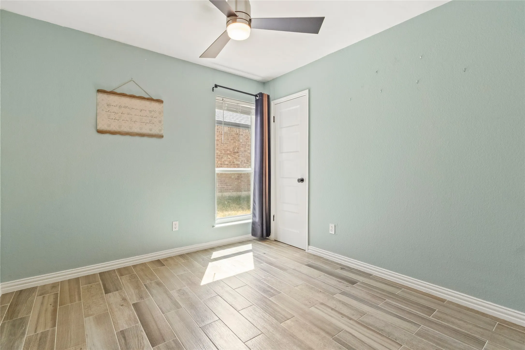Wood-finish flooring, a ceiling fan with integrated lighting, and a window with blinds and dark curtains