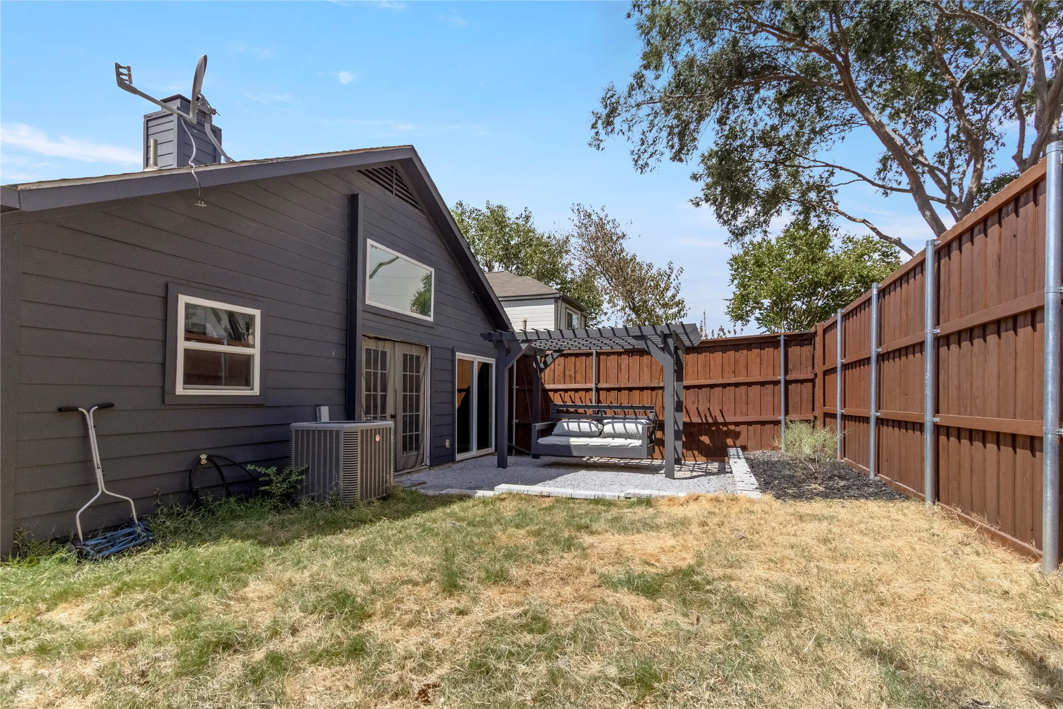 Private backyard featuring wood fencing, a dedicated gravel patio area, a dark-stained swing, and a windowed exterior