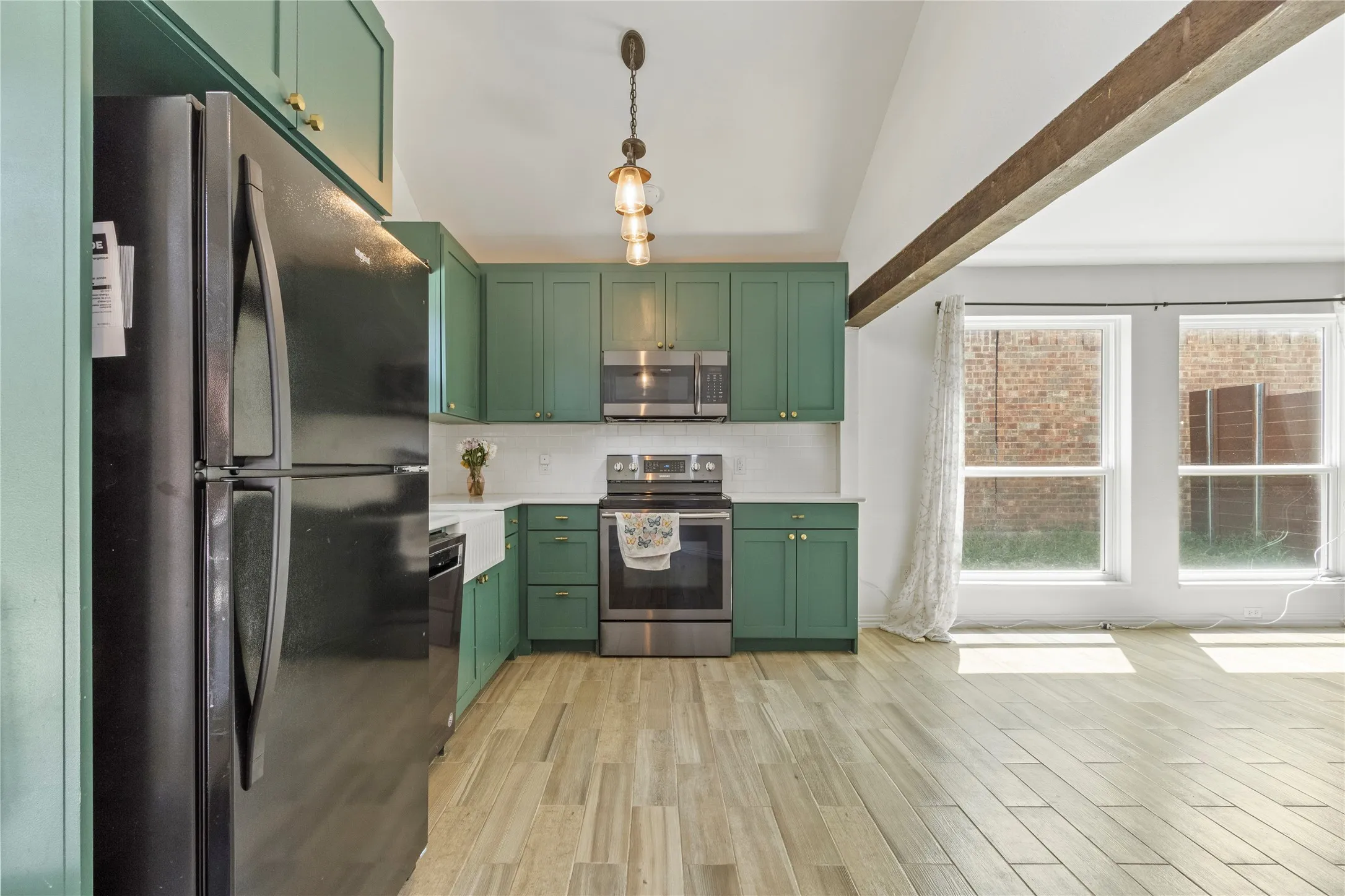 Kitchen featuring green cabinetry, stainless steel appliances, a farmhouse sink, and wood-finish flooring