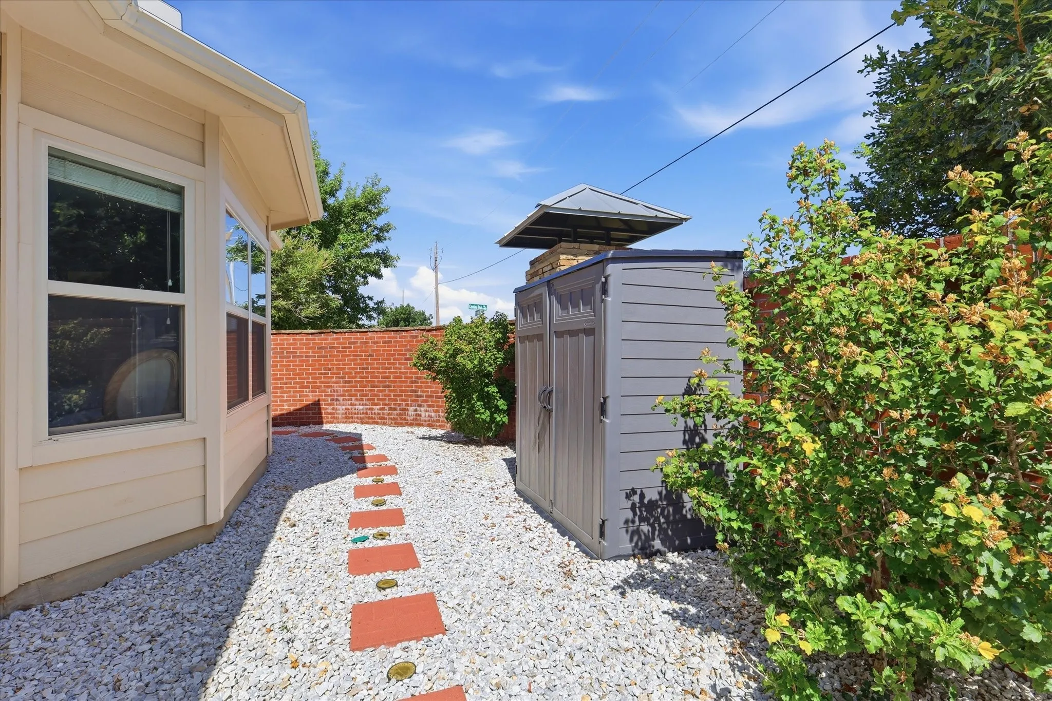 Side yard with gravel, custom pavers and brick fencing - storage building