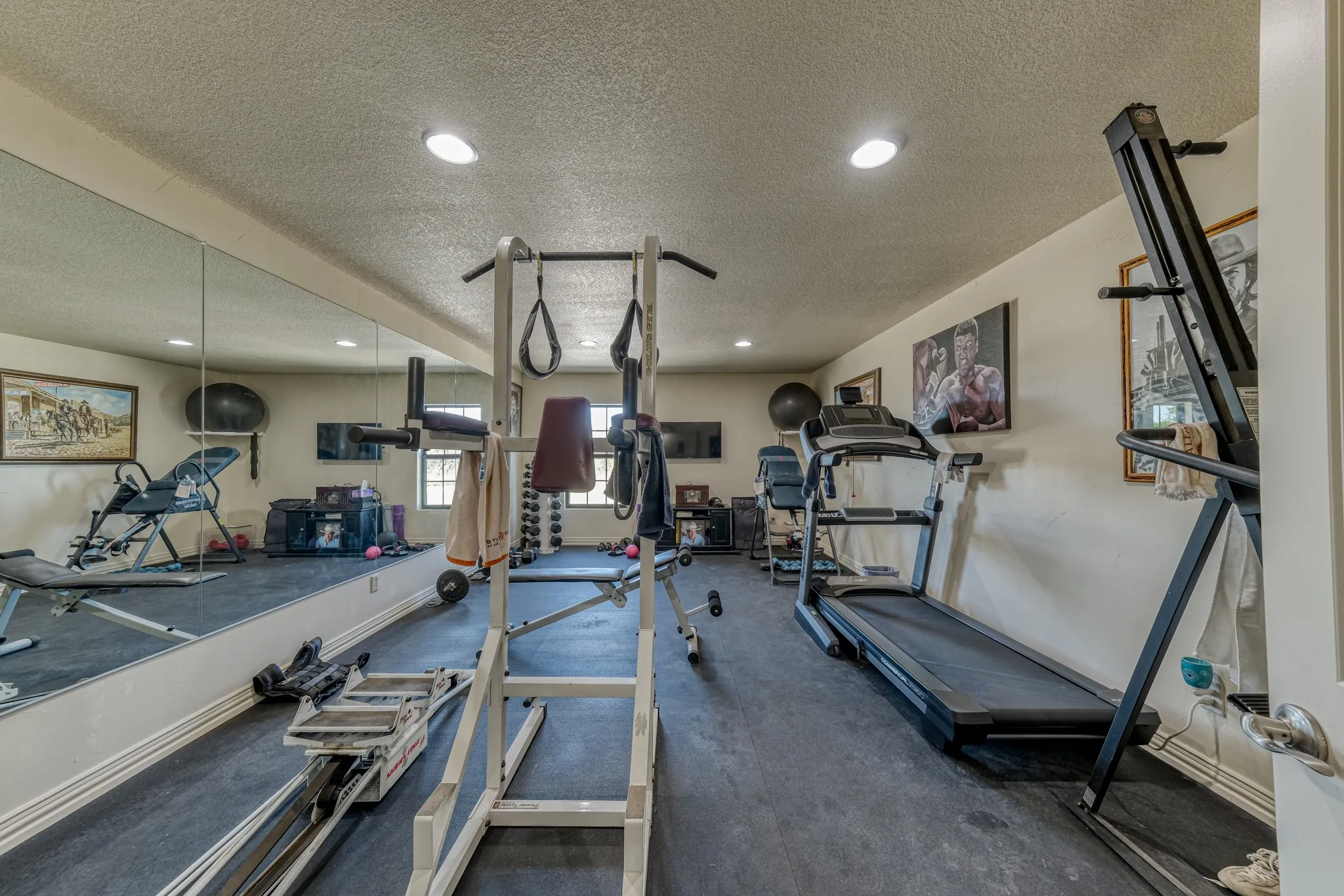 Dedicated fitness room featuring dark rubber flooring, recessed lighting, and a full wall of mirrors