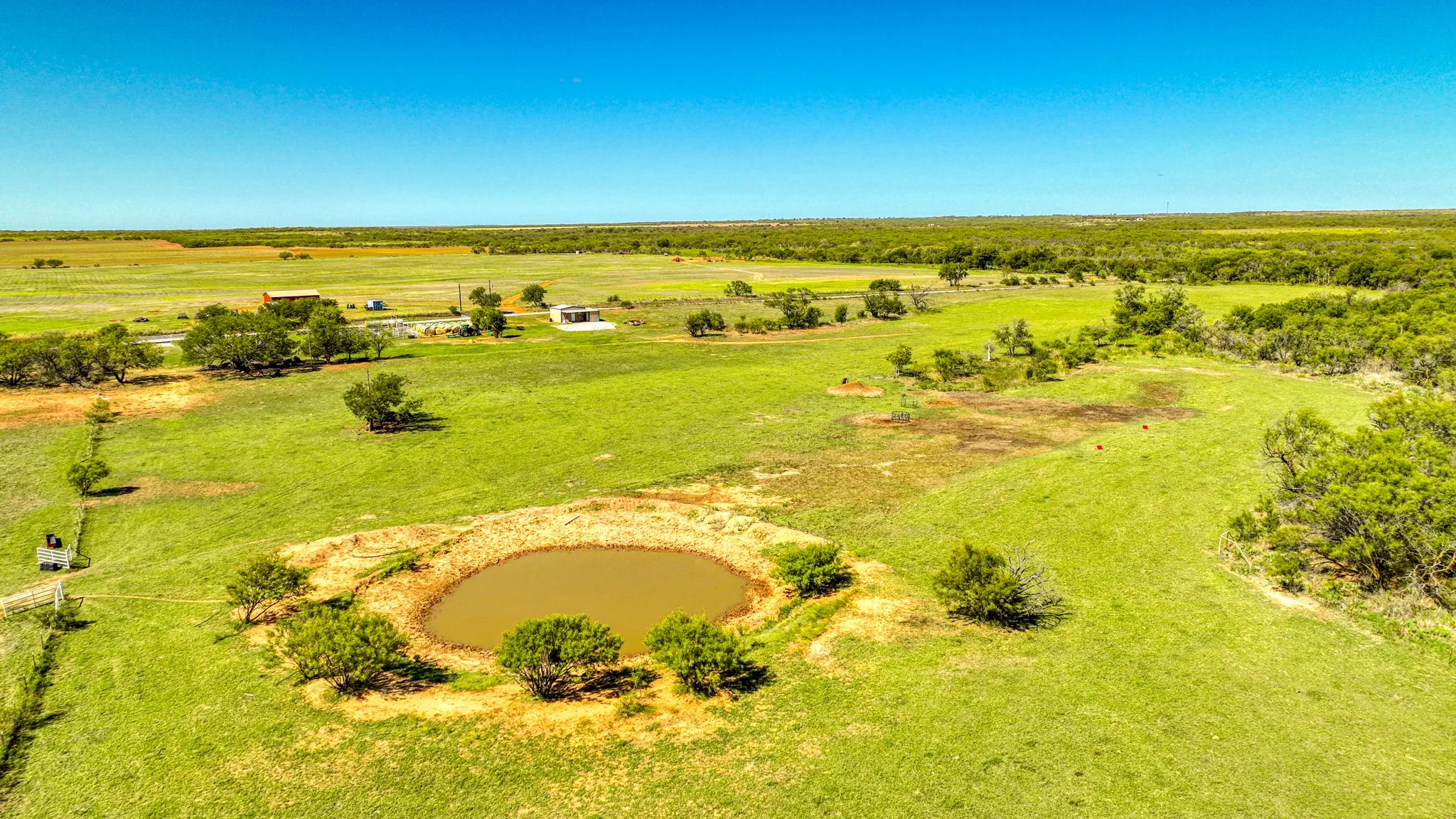 Expansive acreage featuring a central pond with surrounding trees, multiple outbuildings, and a large open field