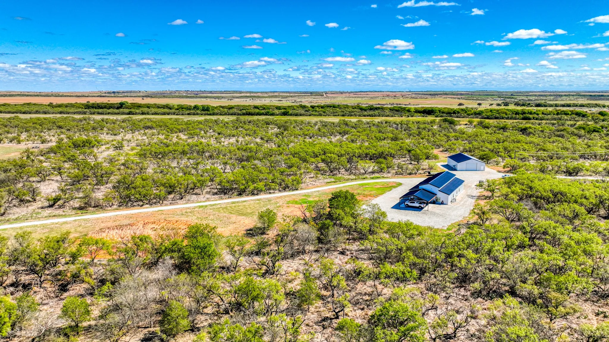 Expansive rural property featuring a modern residence with a dark-pitched roof and an accompanying outbuilding