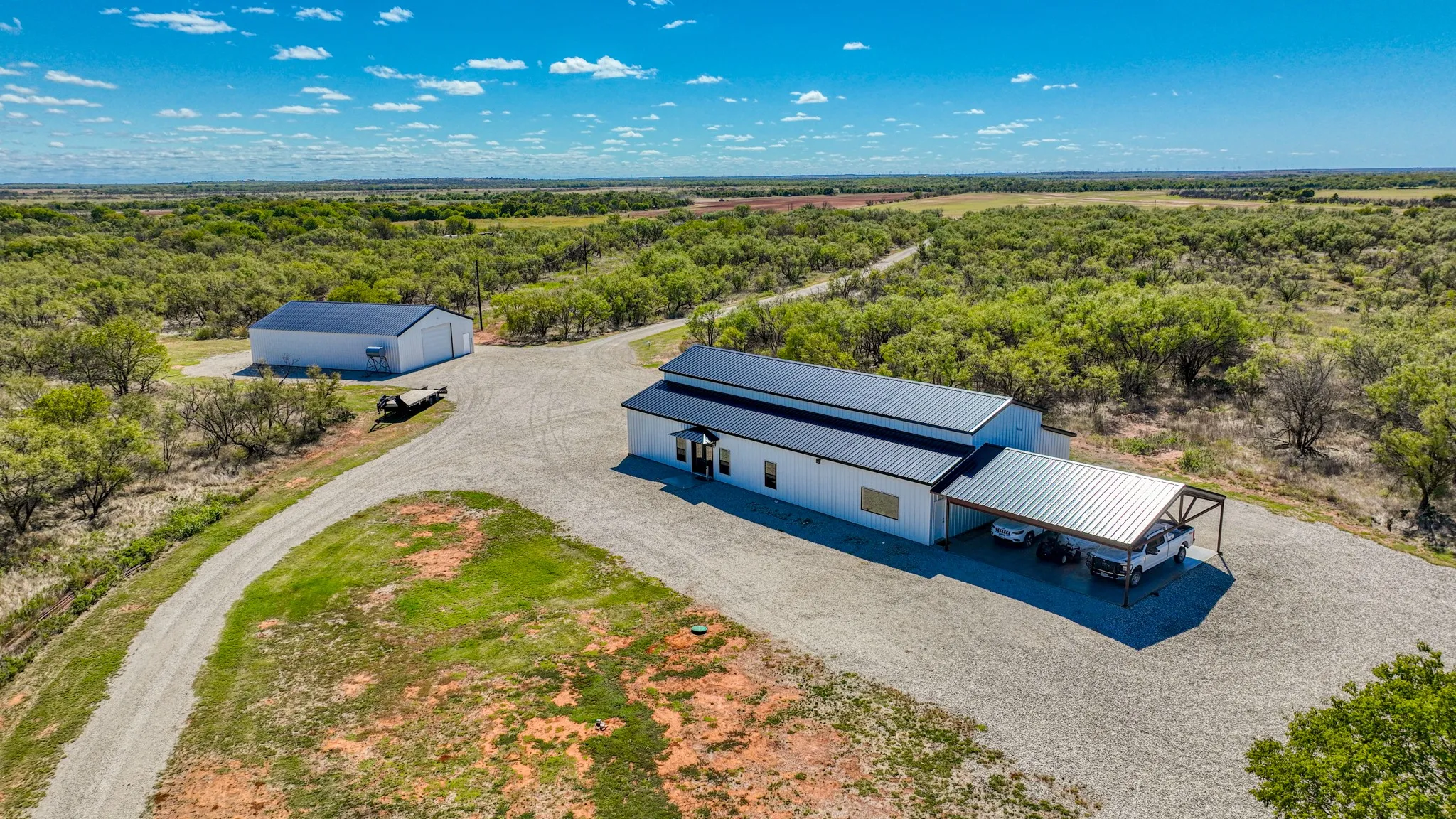 Expansive property featuring a primary residence with a metal roof and attached carport, a separate large outbuilding, and a gravel driveway