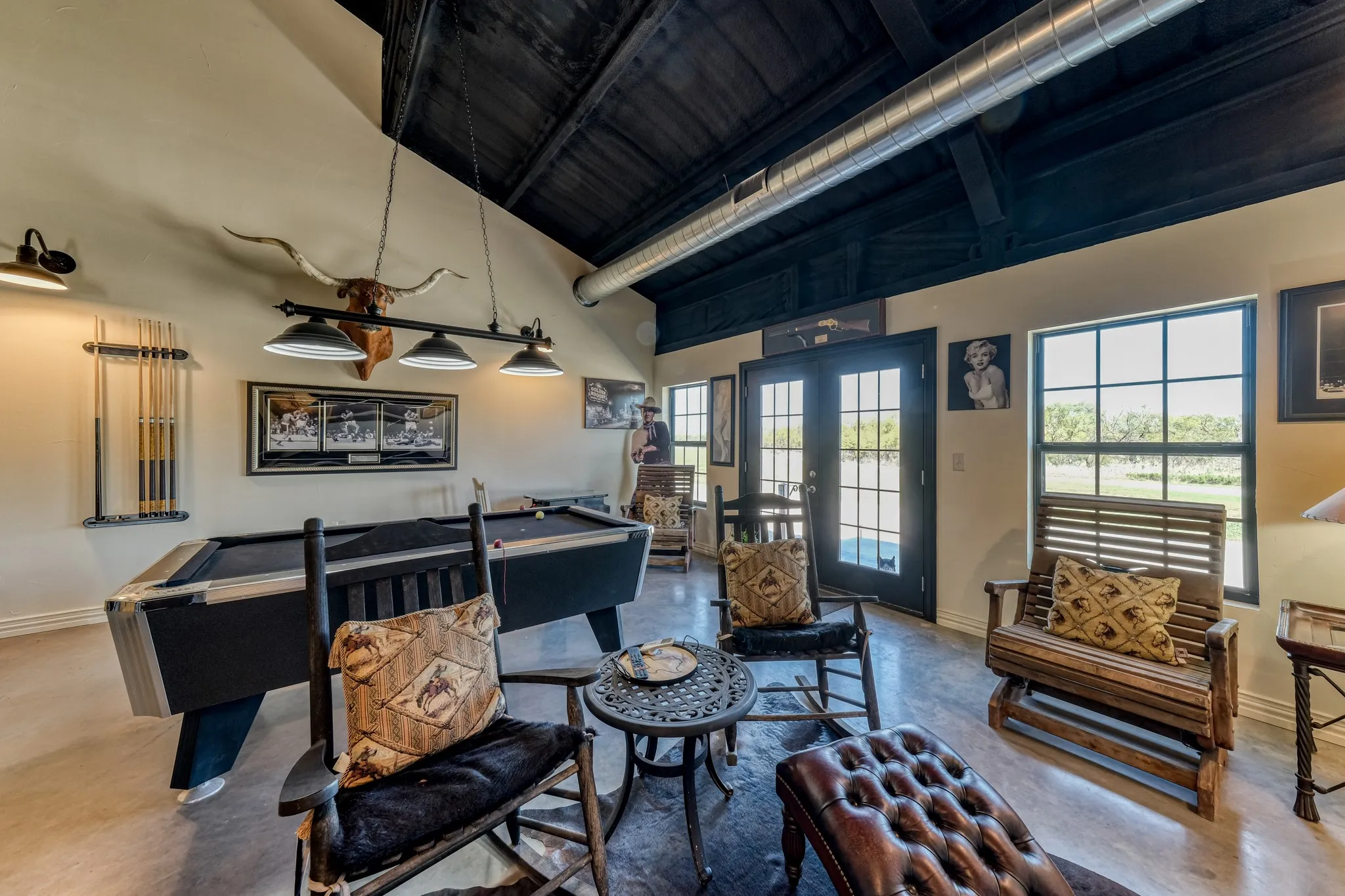 Spacious entertainment area featuring vaulted ceilings with exposed beams, polished concrete flooring, and double French doors with transom windows
