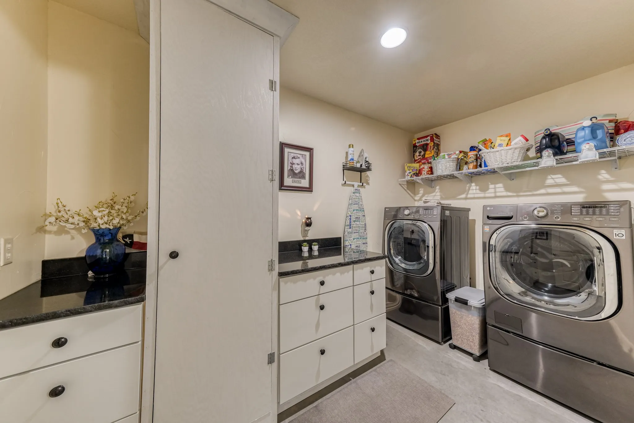 Dedicated laundry area featuring a built-in countertop with dark stone finish, white cabinetry, integrated sink, and overhead shelving