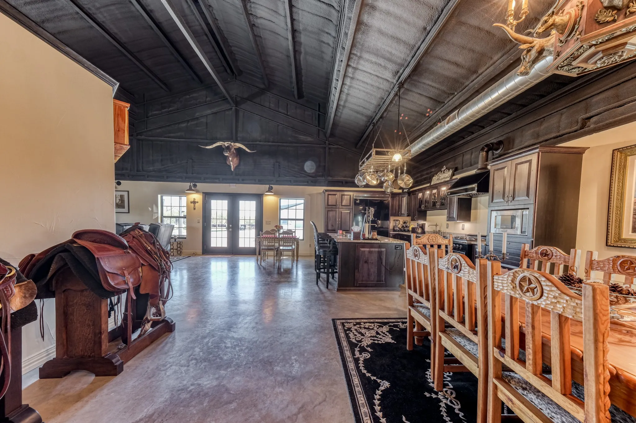 Vaulted ceiling with exposed dark wood beams, polished concrete flooring, kitchen with dark wood cabinetry, kitchen island with seating, and double glass-paneled exterior doors