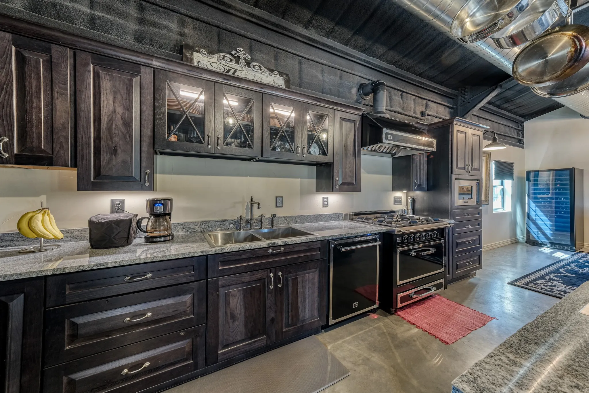 Kitchen featuring dark wood cabinetry, light-colored countertops, a stainless steel sink with a gooseneck faucet, a built-in dishwasher, and a professional-grade range with a matching range hood