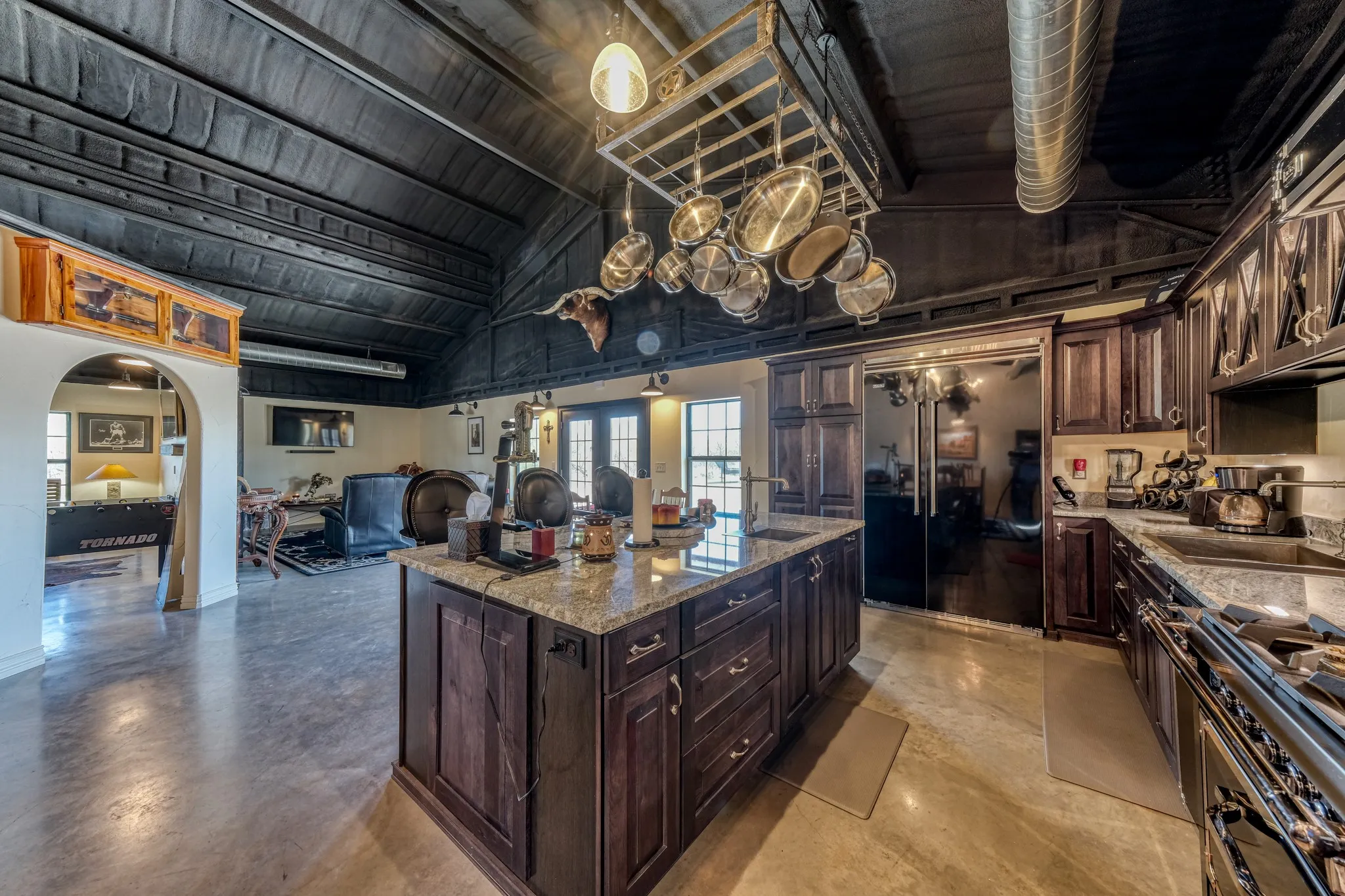Spacious kitchen featuring a large central island with a light-toned countertop, dark wood cabinetry, and stainless steel appliances