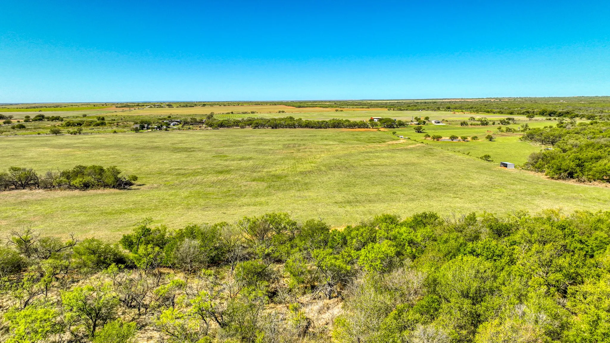 Expansive landscape featuring open grassy fields, diverse tree coverage, and a distant structure