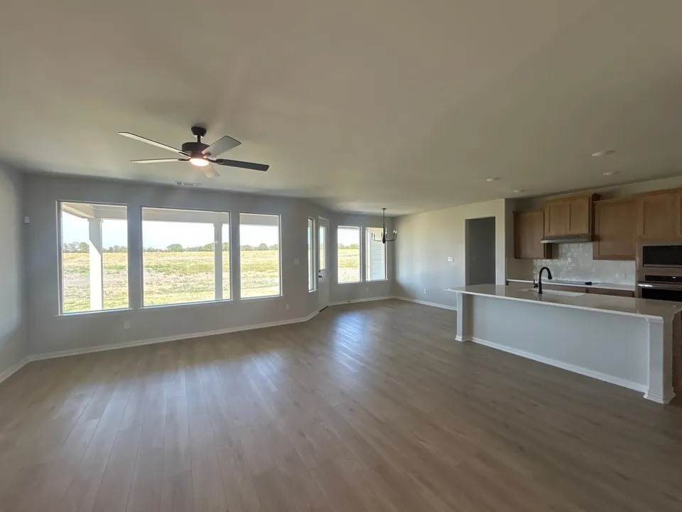 Wood-finish flooring throughout, with a multi-pane window wall, ceiling fan, and kitchen island featuring a sink and black faucet