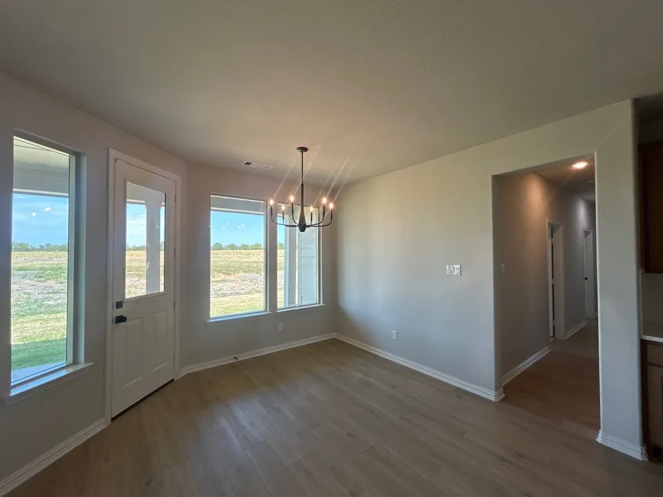 Light wood-finish flooring, multiple windows, a glass-paneled door, and a black chandelier