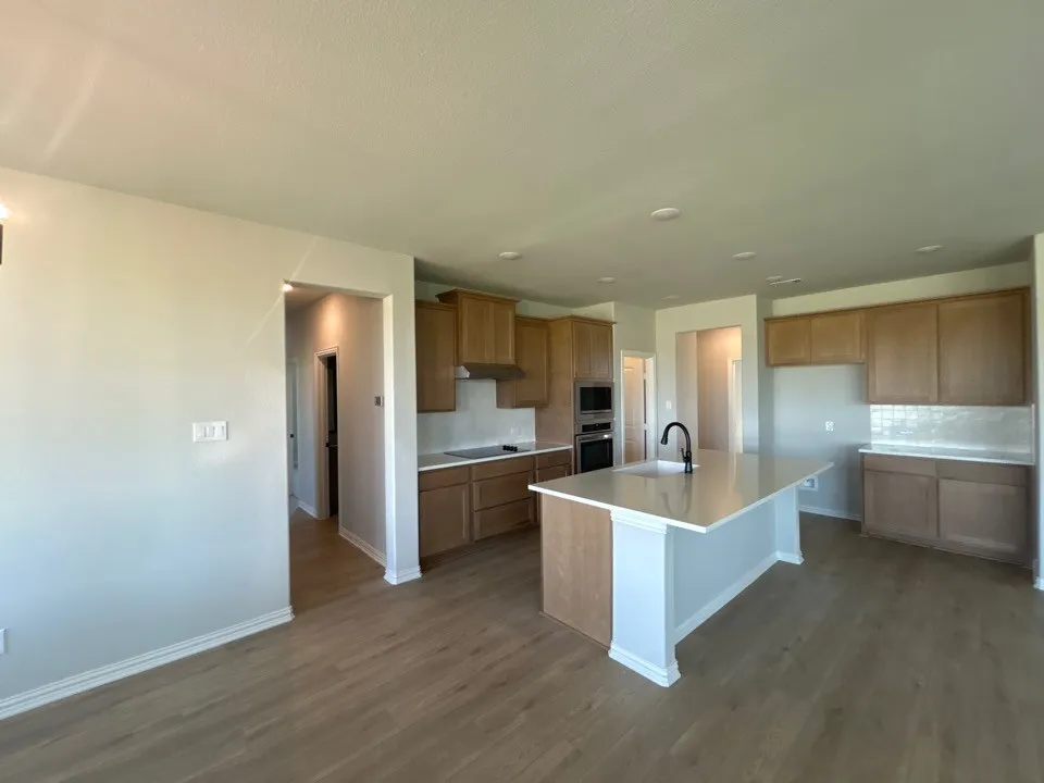 Kitchen featuring wood-finish flooring, recessed lighting, a central island with an undermount sink and matte black faucet, light wood-tone cabinetry, and a subway tile backsplash