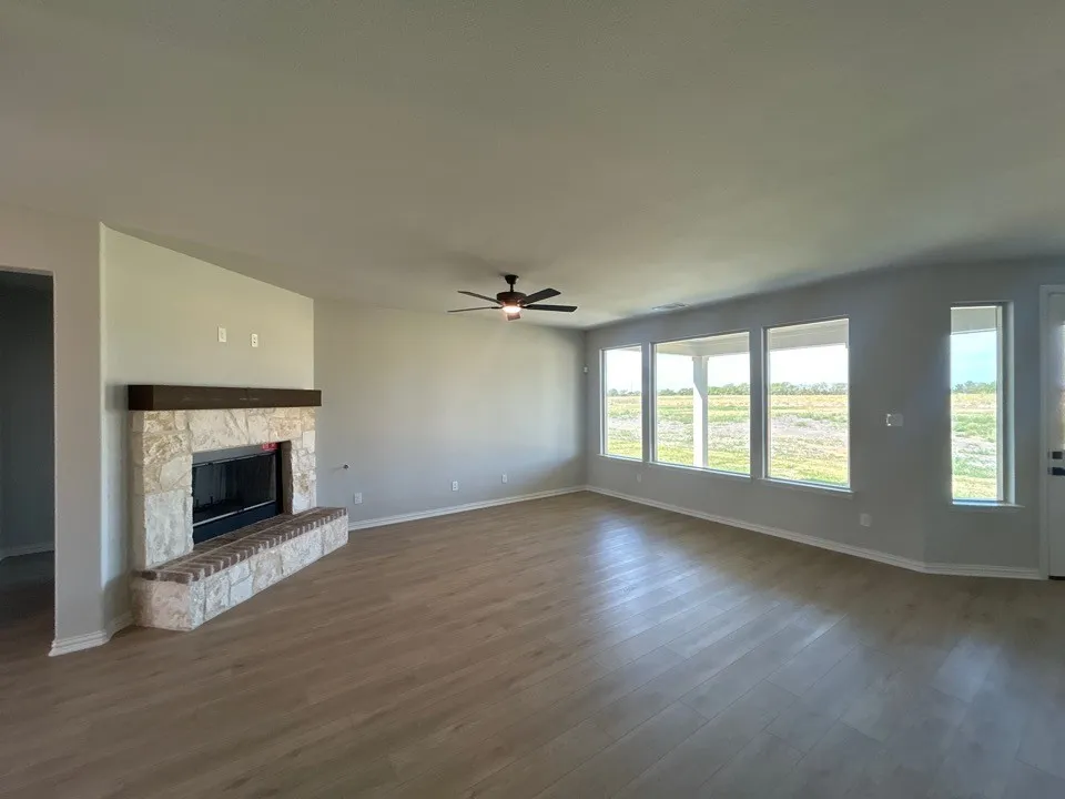 Spacious room featuring wood-finish flooring, a stone-clad fireplace with a hearth, multiple windows, and a ceiling fan
