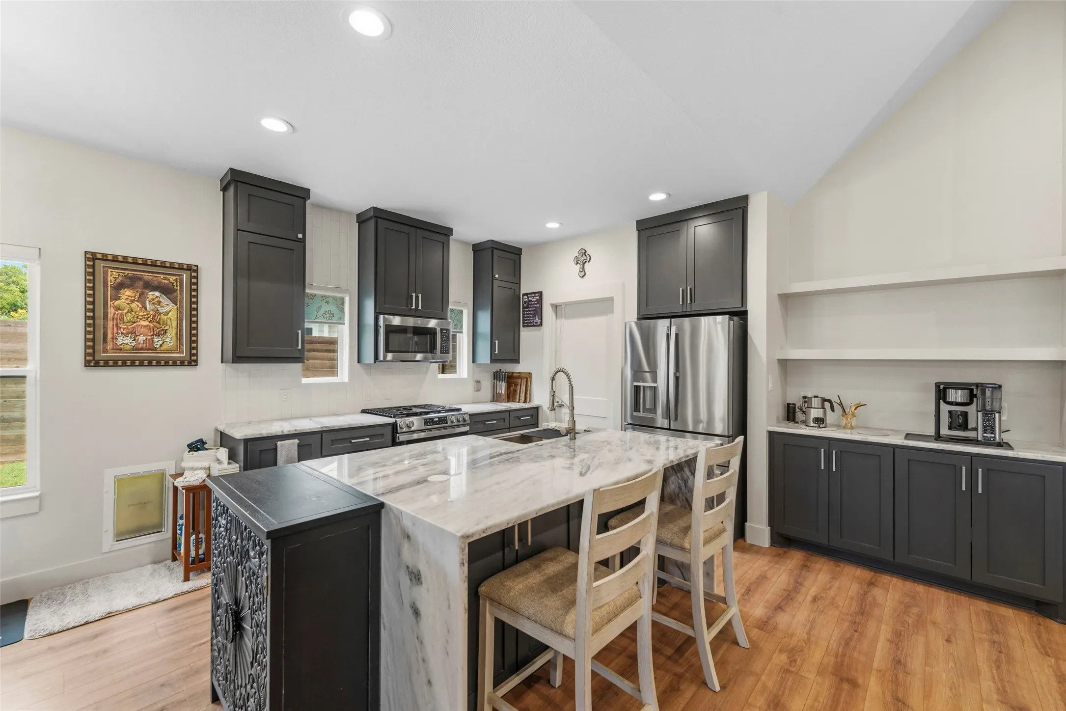 Kitchen featuring a large waterfall island with integrated seating, dark cabinetry, stainless steel appliances, and wood-finish flooring