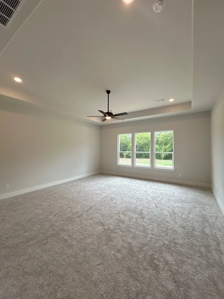 Spacious room with tray ceiling, recessed lighting, ceiling fan, and triple windows