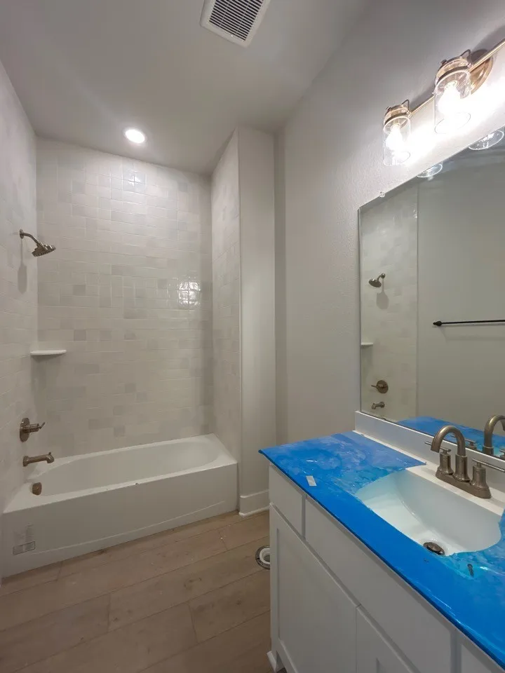 Bathroom featuring a tub/shower combination with subway tile surround, wood-finish flooring, a single vanity with an integrated sink, and an overhead vanity light fixture