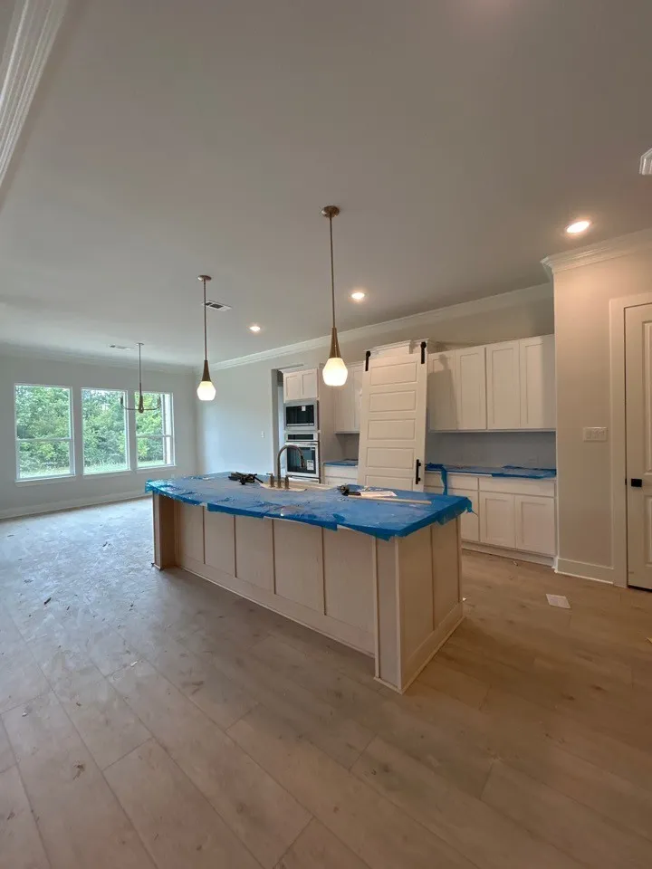 Wood-finish flooring, white cabinetry, built-in double ovens, and a kitchen island with paneling detail