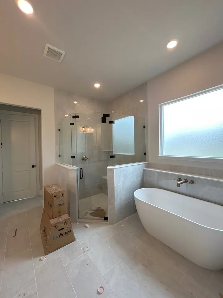 Freestanding soaking tub with wall-mounted faucet, glass-enclosed shower with tile surround, and recessed lighting