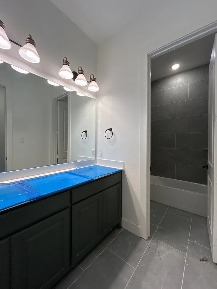 Double vanity with dark cabinetry, wall-mounted lighting, and a large mirror
