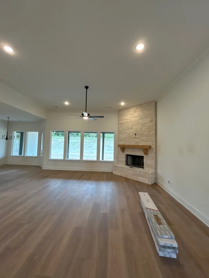Spacious room featuring wood-finish flooring, a stone fireplace with a wood mantle, recessed lighting, a ceiling fan, and multiple windows