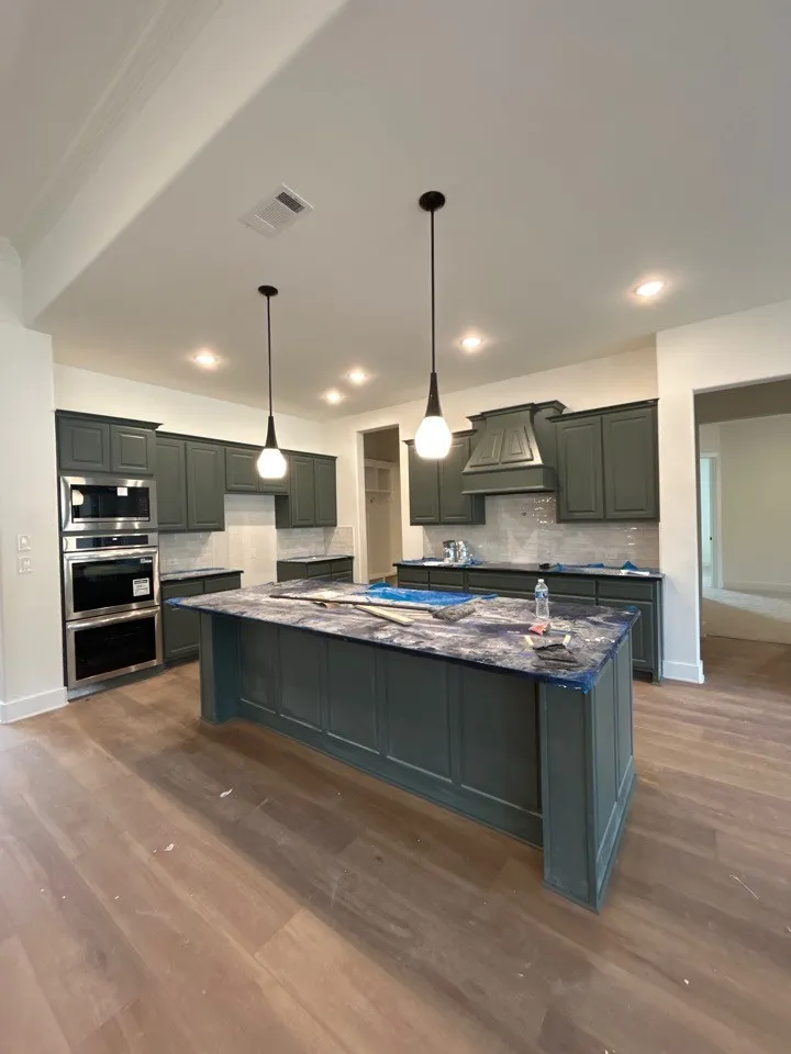 Kitchen featuring dark-toned cabinetry, a spacious central island, wood-finish flooring, recessed lighting, and stainless steel built-in double ovens