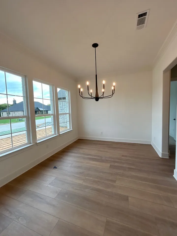 Spacious room featuring wood-finish flooring, ample natural light through multiple windows, and a modern chandelier
