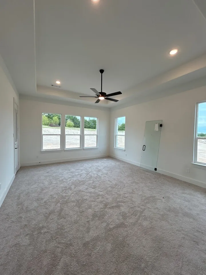 Tray ceiling with recessed lighting and a ceiling fan, three pane windows, carpet flooring, and a clear glass door