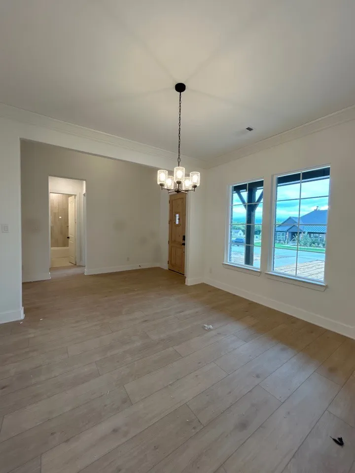 Wood-finish flooring throughout, modern chandelier, double windows with white trim, and a light wood-paneled door