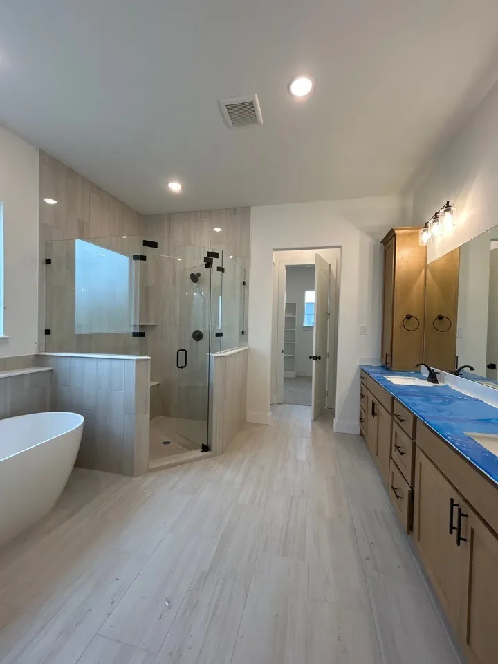 Walk-in shower with clear glass enclosure, freestanding soaking tub, dual vanity with undermount sinks, wood-finish flooring, and recessed lighting