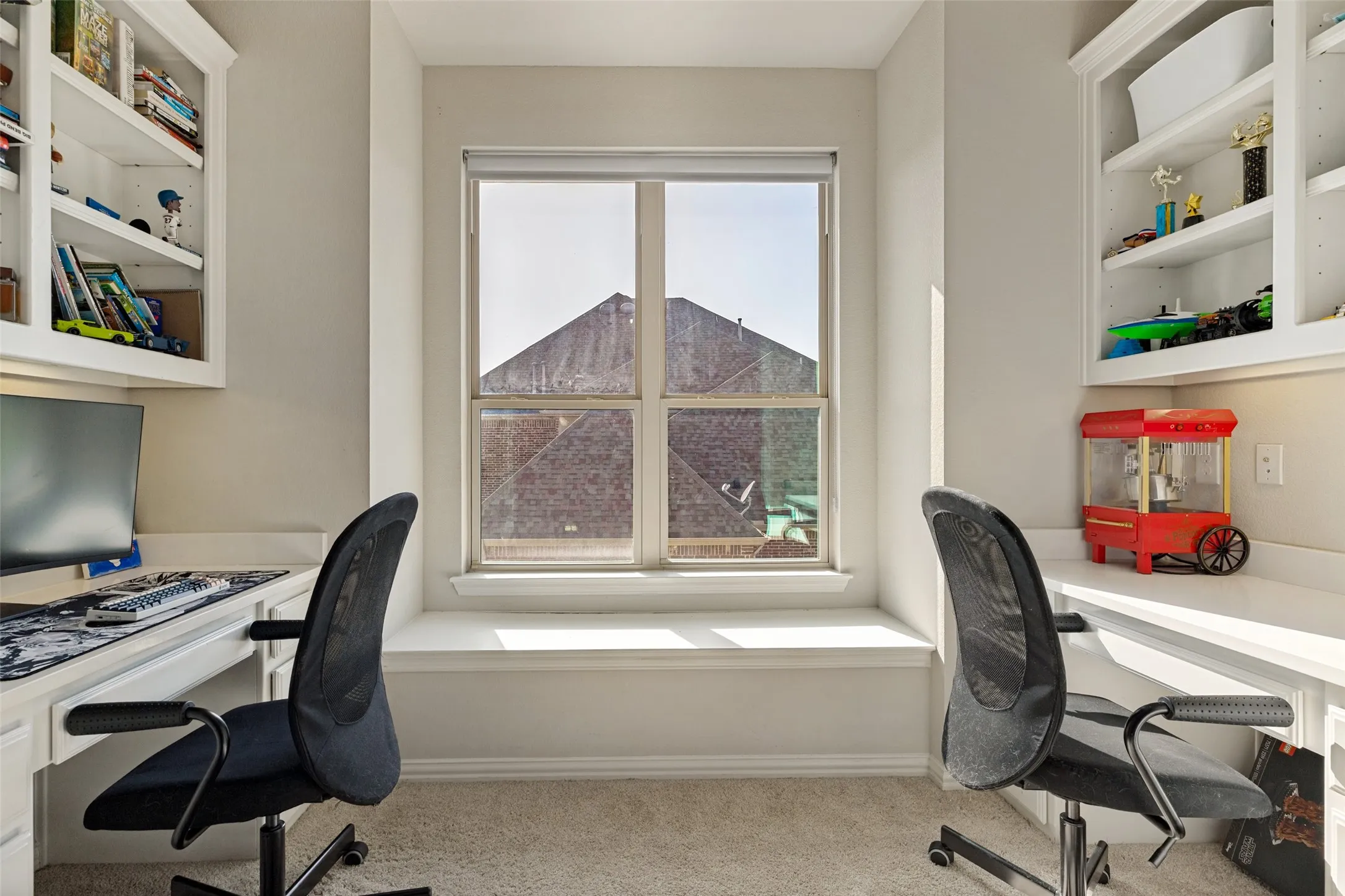 Built-in desk area featuring two workstations with integrated shelving, a window with a deep sill, and neutral carpeting