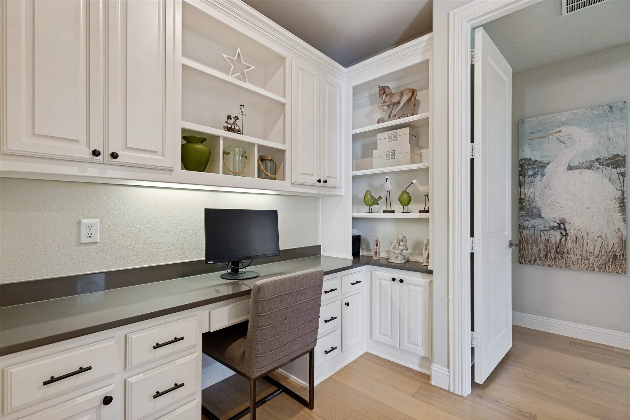 Built-in desk area featuring white cabinetry, a dark countertop, under-cabinet lighting, and light wood-finish flooring