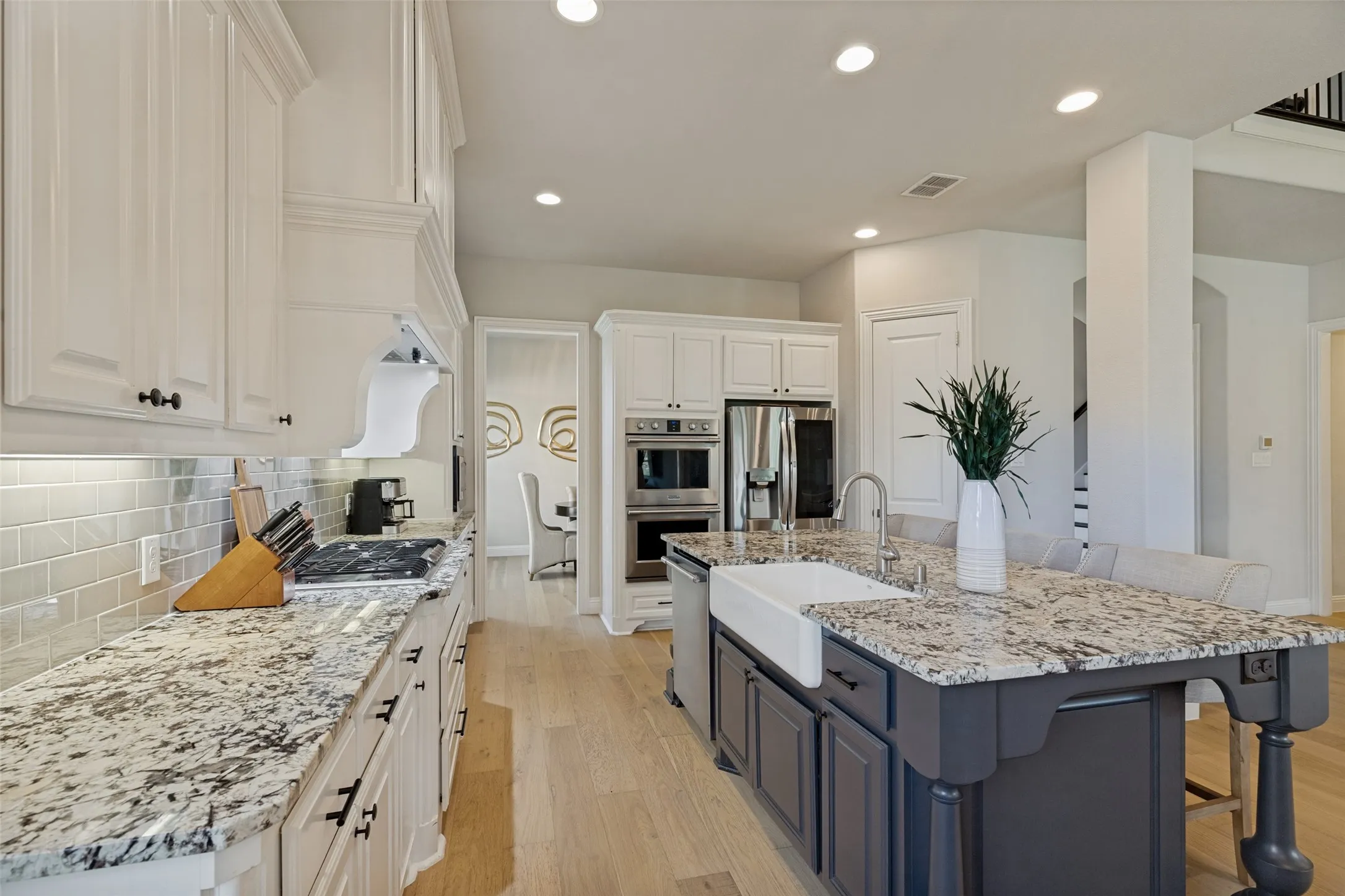 Modern kitchen featuring a two-toned island with a farmhouse sink, light wood-finish flooring, white cabinetry, integrated stainless steel appliances, and subway tile backsplash