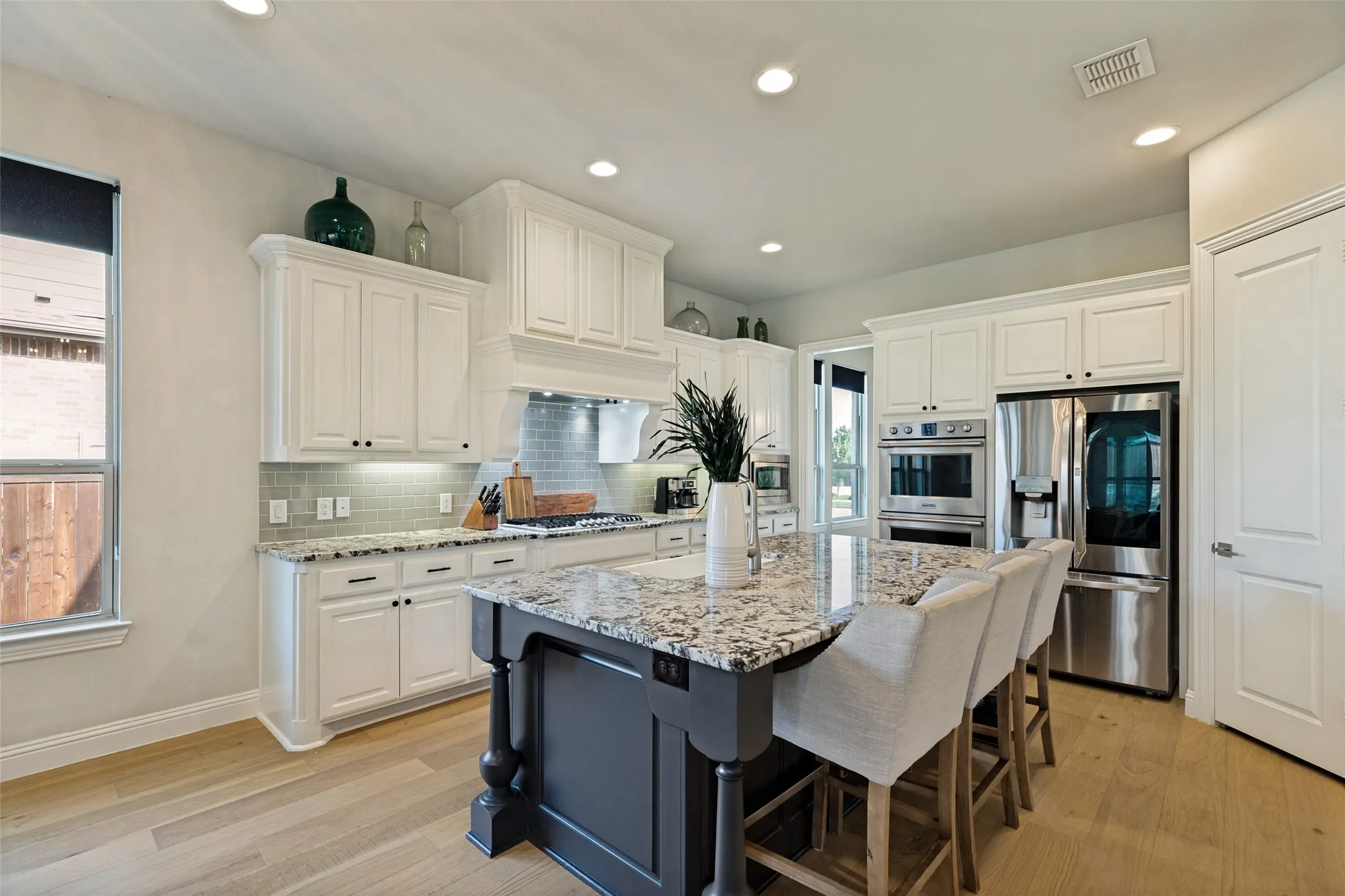 Gourmet kitchen featuring a substantial island with seating, a smooth cooktop, stainless steel built-in appliances, ample white cabinetry, and light wood-finish flooring