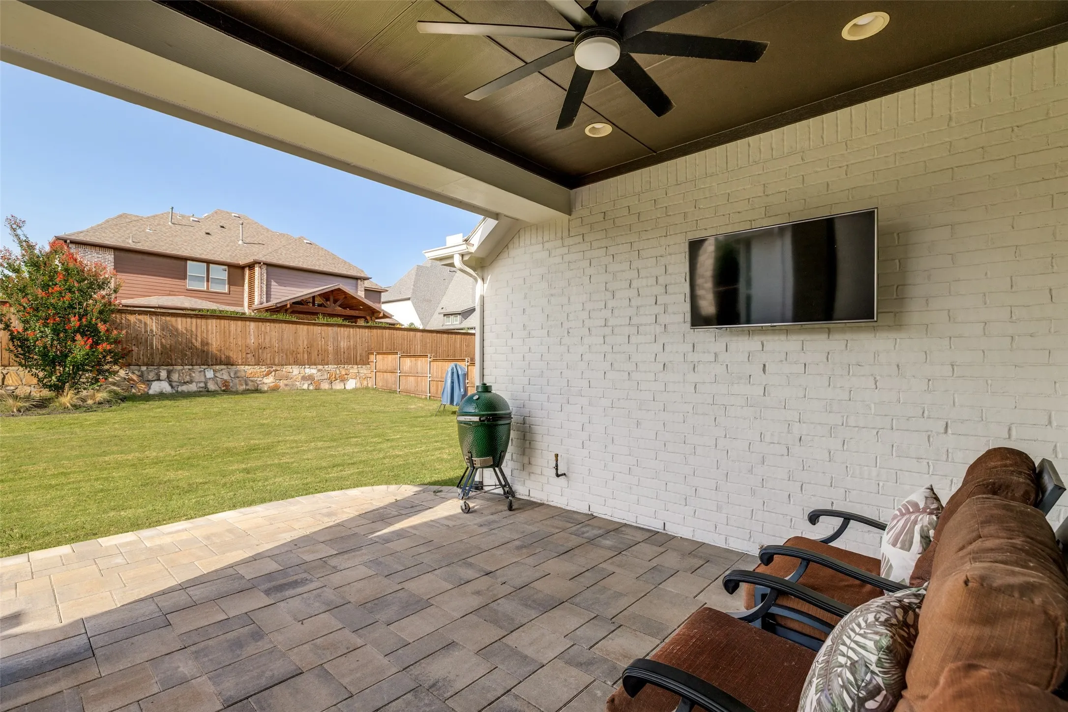 Covered outdoor patio featuring a paver stone surface, white painted brick wall, and a dark wood-finish ceiling with a ceiling fan