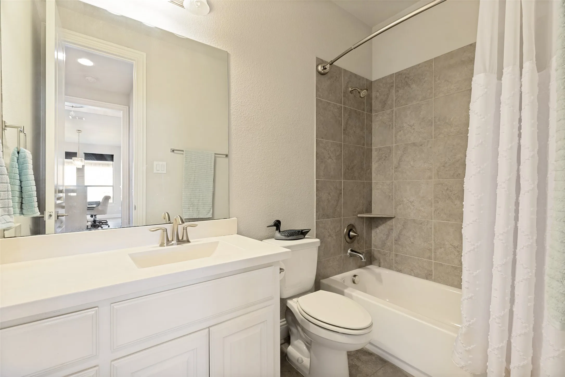Bathroom featuring a white vanity with an integrated sink, brushed nickel faucet, a large wall-mounted mirror, and a tiled shower-tub combination with a built-in shelf