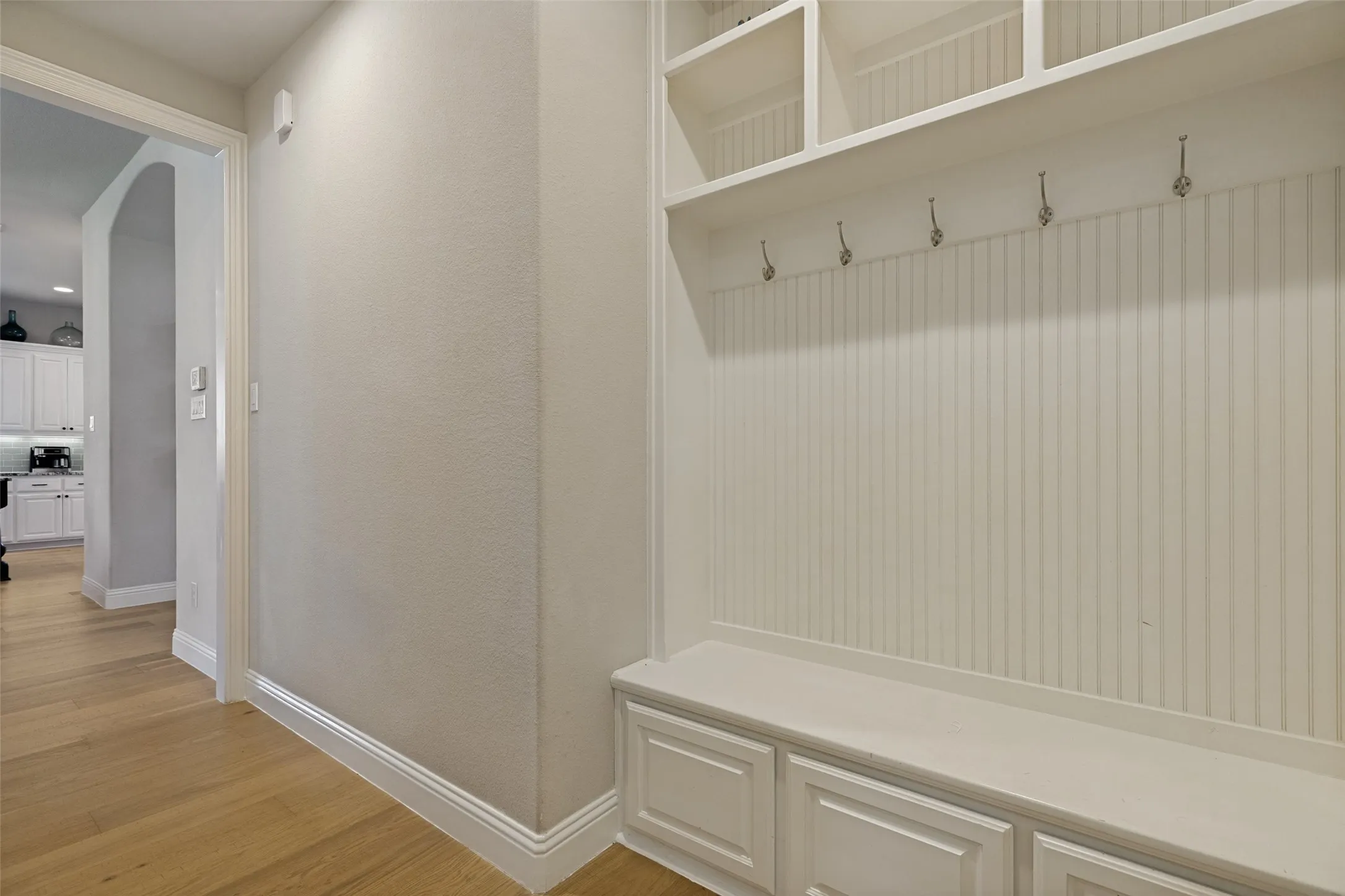 Built-in mudroom bench with paneled cabinetry, open shelving, beadboard backing, and metal coat hooks