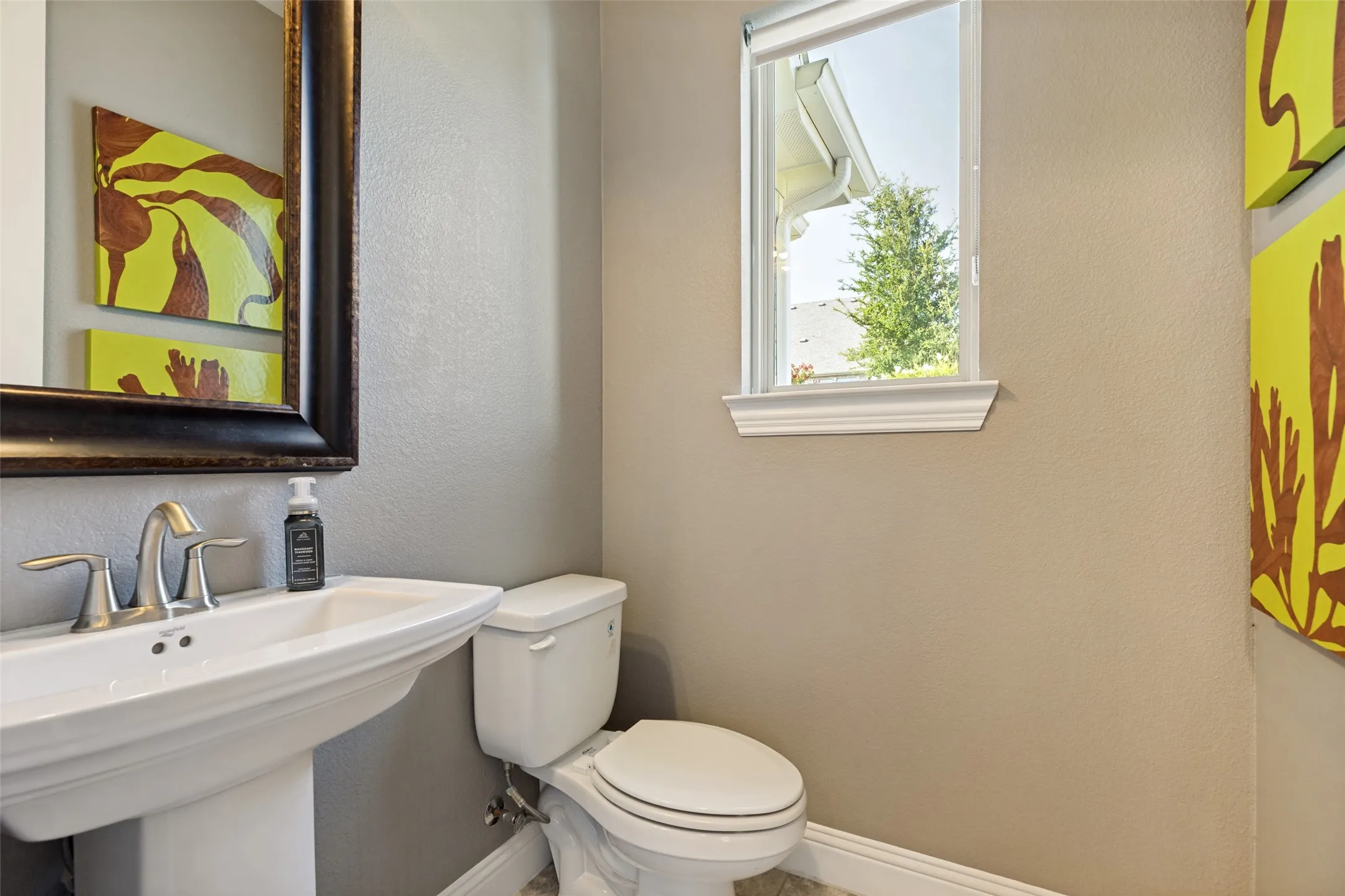 Pedestal sink with a polished chrome faucet, framed mirror, and a window with white trim