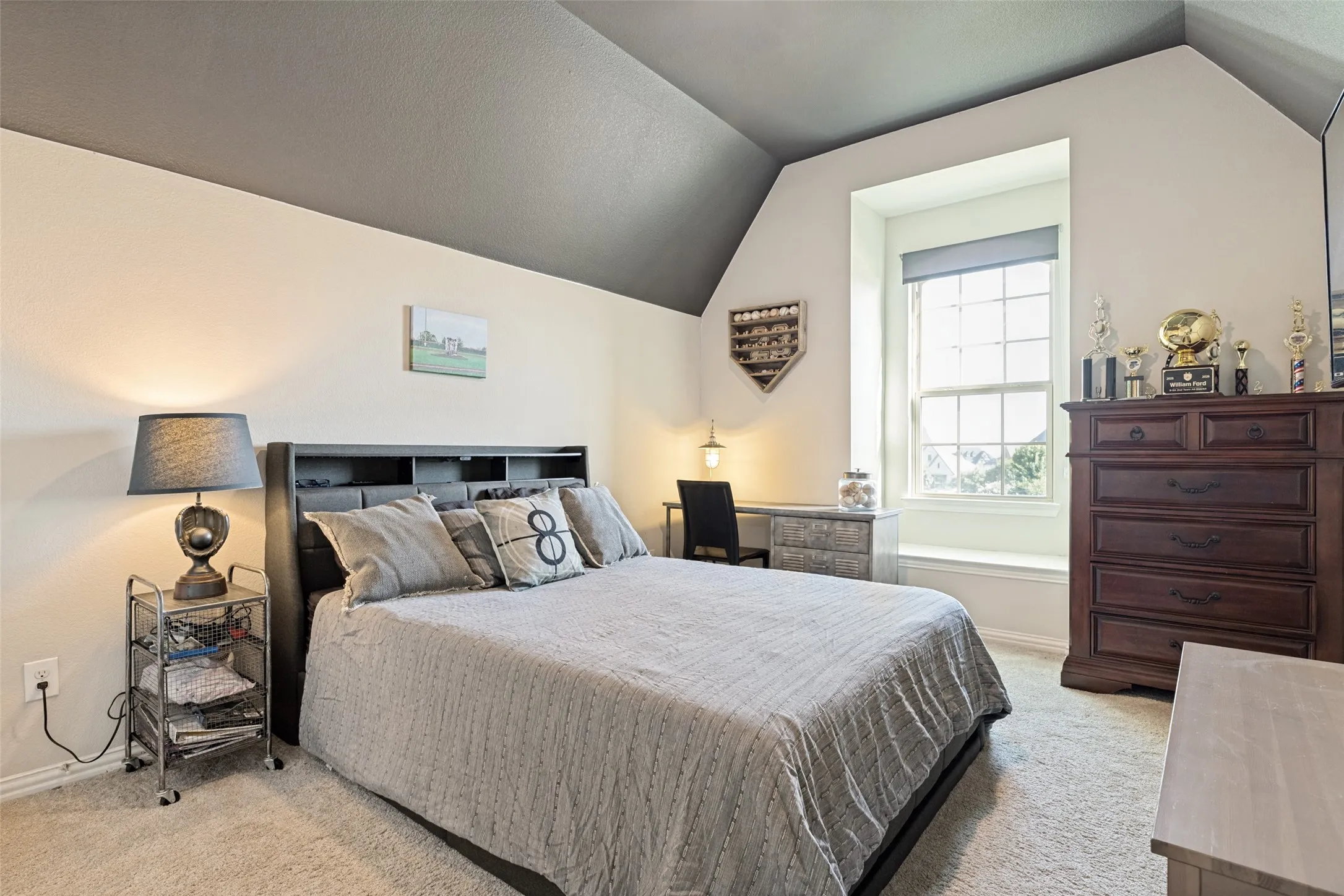 Carpeted room featuring a window with a deep sill, a built-in shelf headboard, a sloped ceiling with a two-tone paint scheme, and a built-in desk area