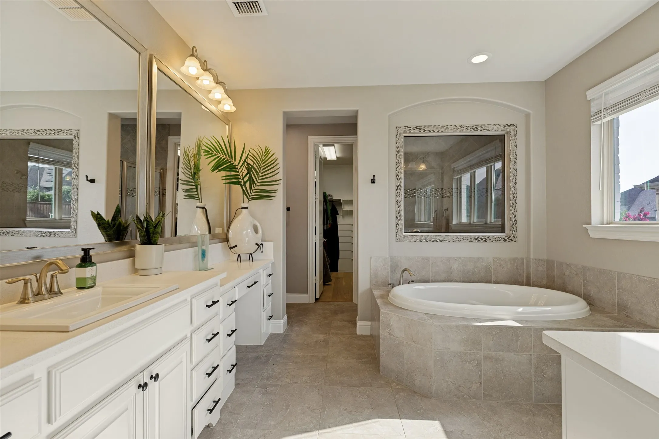 Spacious bathroom featuring a dual vanity with ample storage, a large soaking tub with tiled surround, and a framed mirror