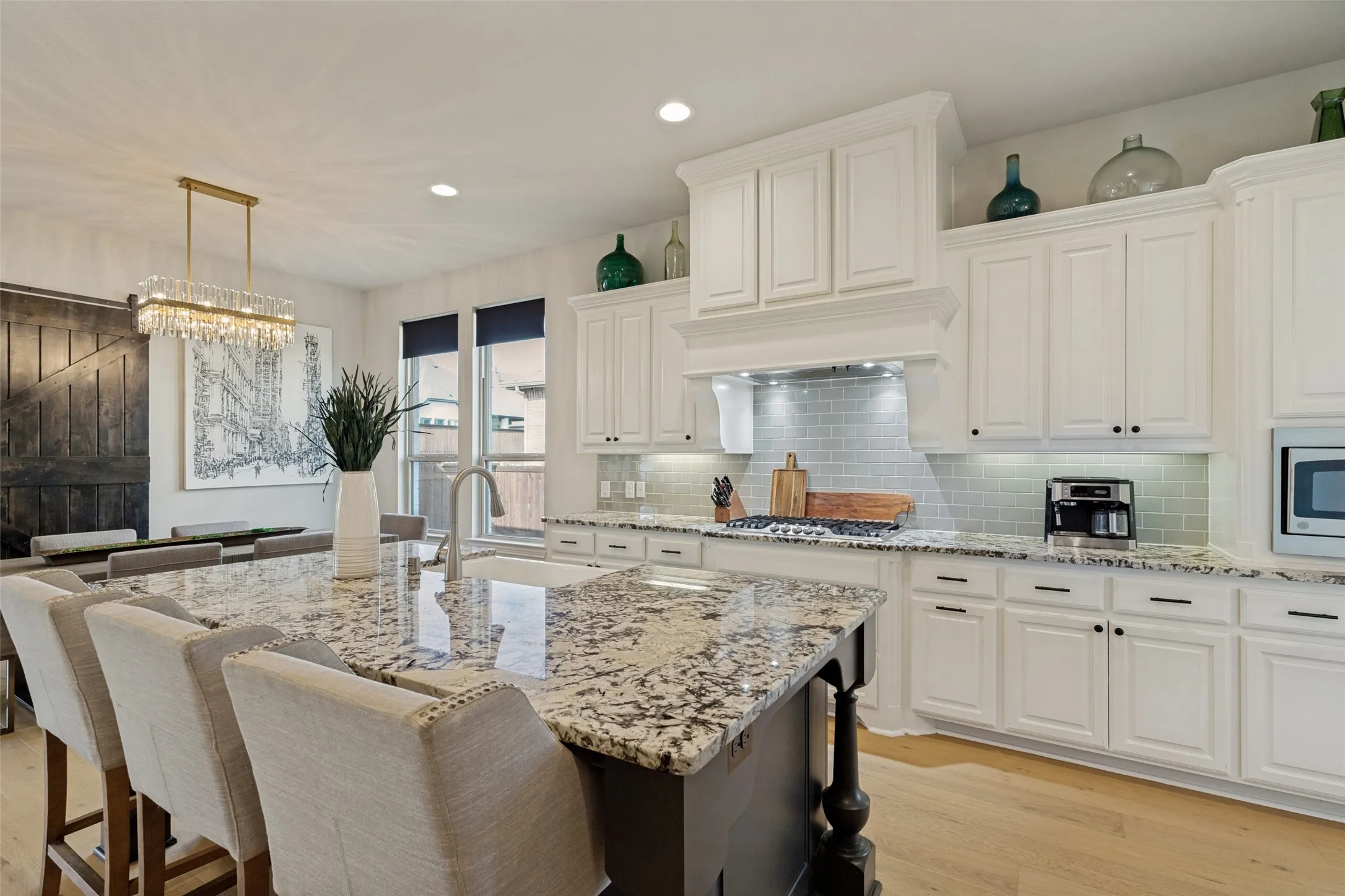 Kitchen featuring a large island with an undermount sink, light wood-finish flooring, white cabinetry, speckled countertops, and a subway tile backsplash