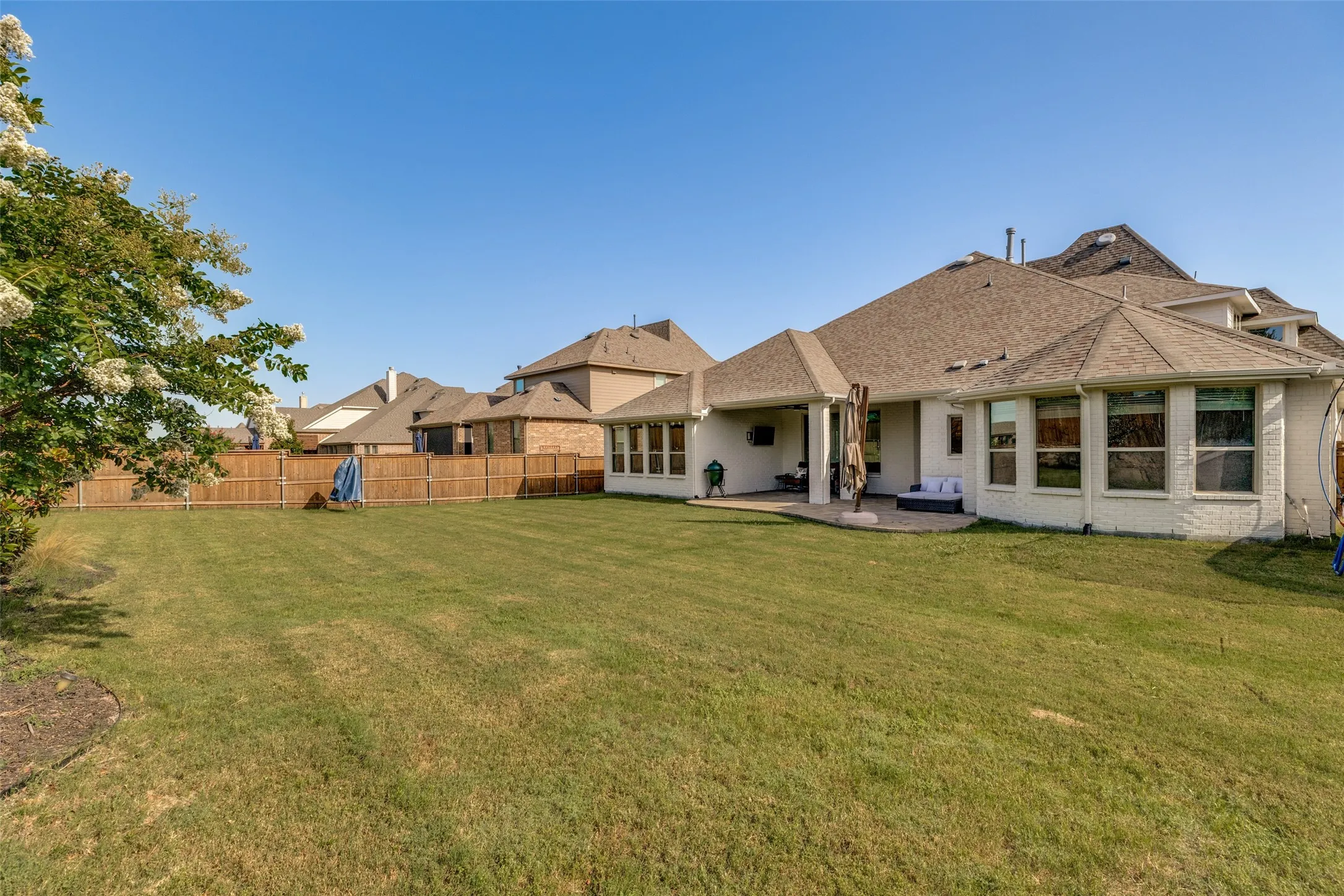 Expansive fenced backyard featuring a generously sized lawn, covered patio, sunroom, and a large multi-level roofline