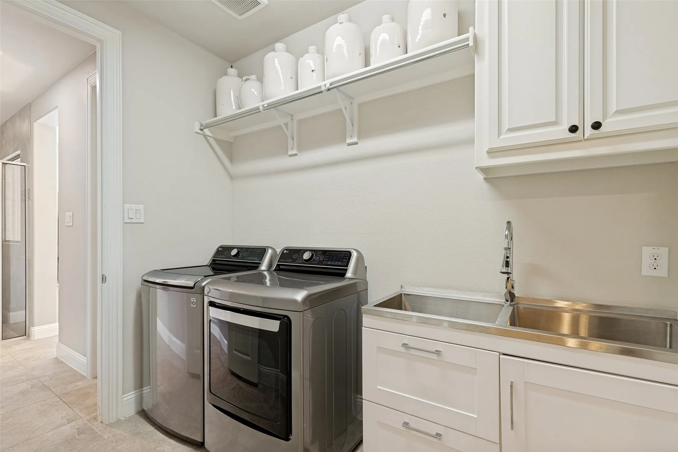 Laundry room featuring a stainless steel dual-basin utility sink, white shaker-style cabinetry, and open shelving