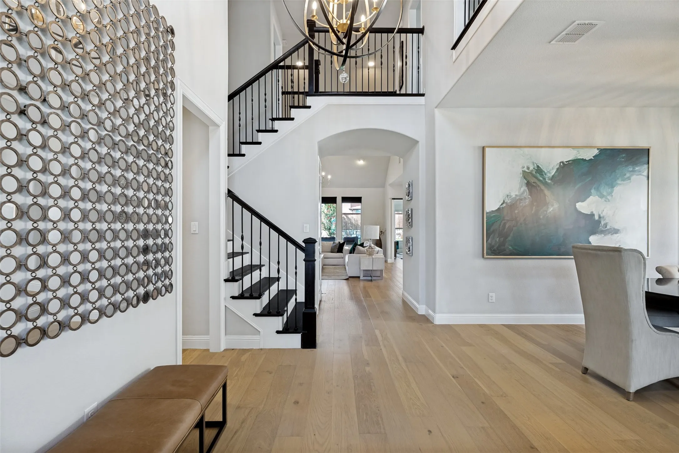 Two-story foyer featuring light wood-finish flooring, a grand staircase with wrought iron balusters, a contemporary chandelier, arched entryways, and crisp white walls