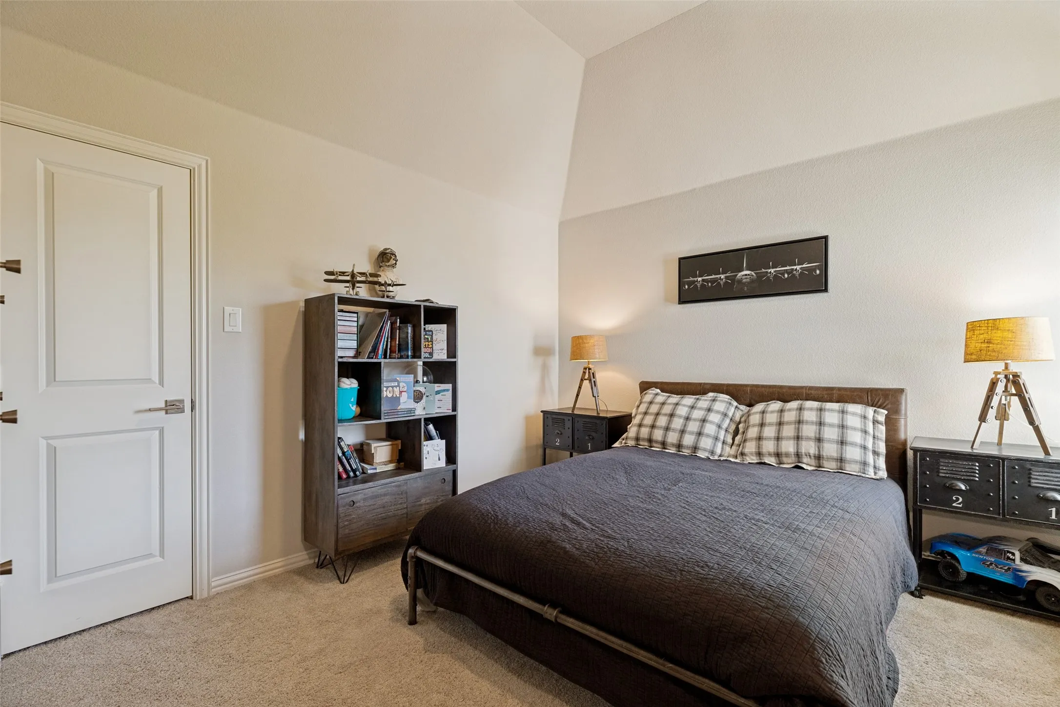 Spacious room featuring vaulted ceilings, neutral-toned carpeting, and a crisp white paneled door with brushed nickel hardware