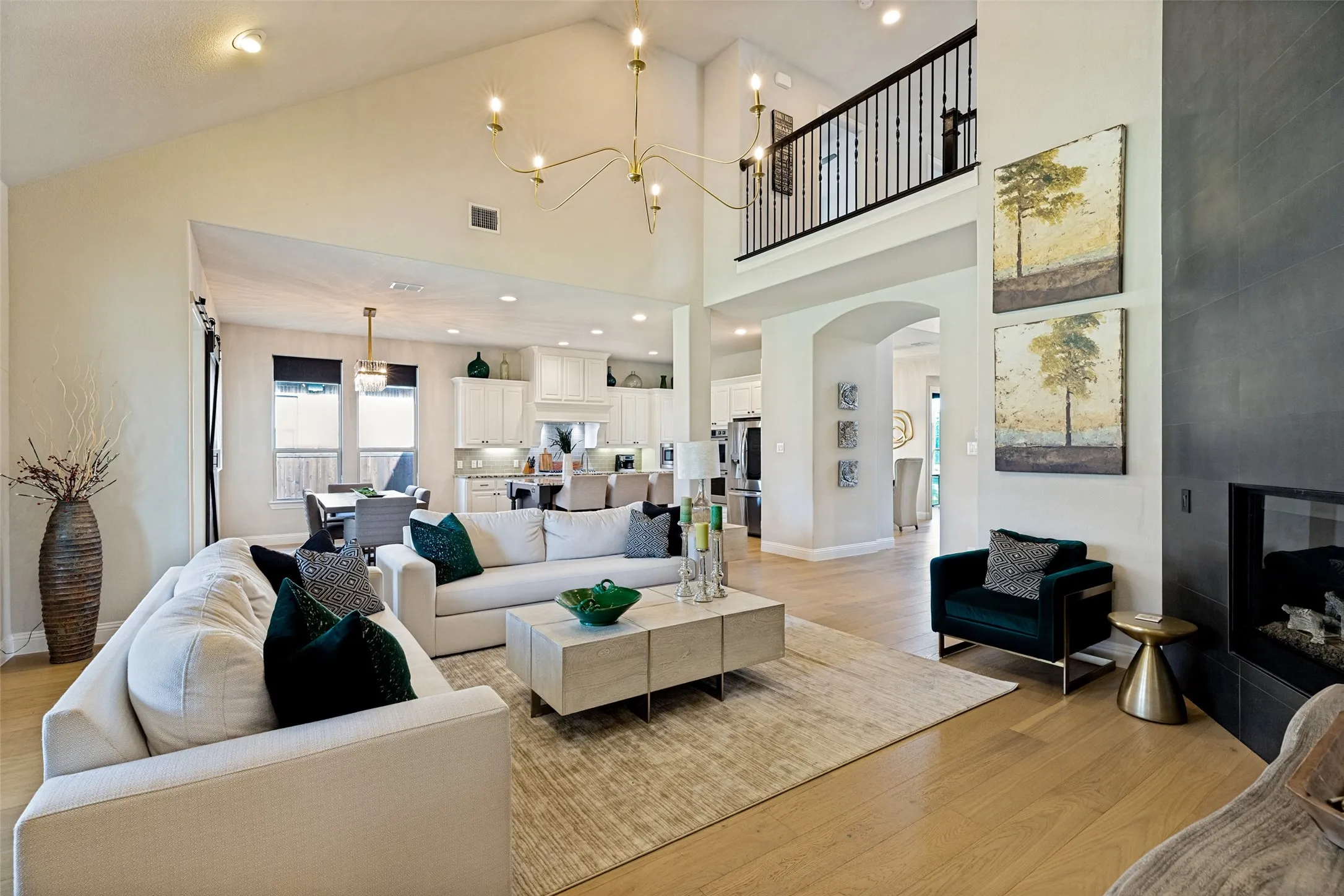 Two-story living area featuring vaulted ceilings, a contemporary chandelier, and light wood-finish flooring