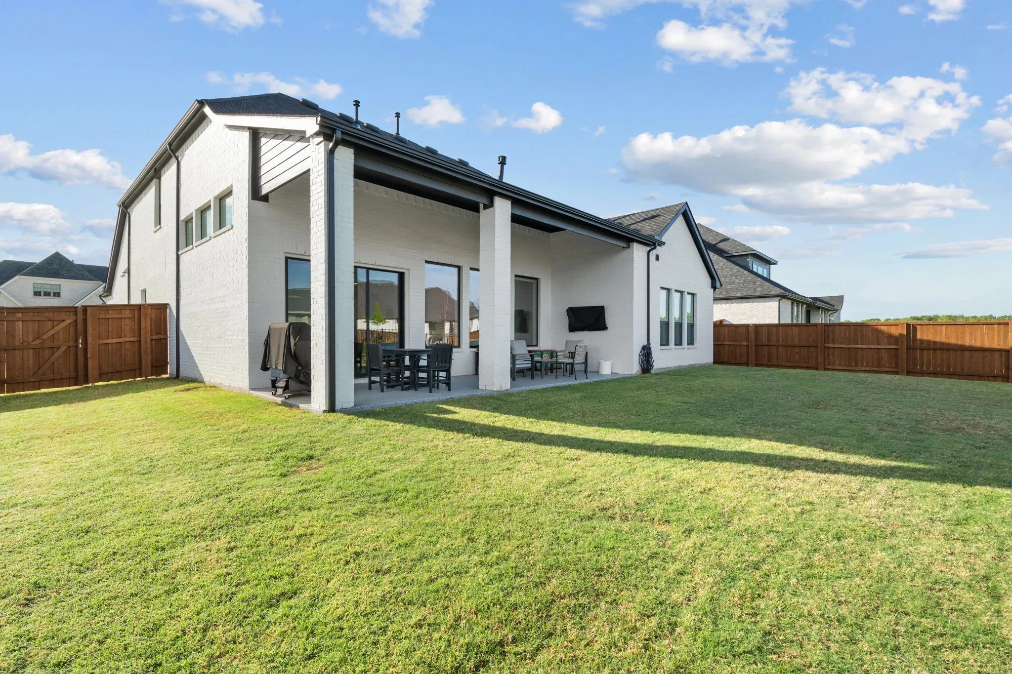 Expansive backyard featuring a covered patio, brick exterior, dark window frames, and perimeter fencing